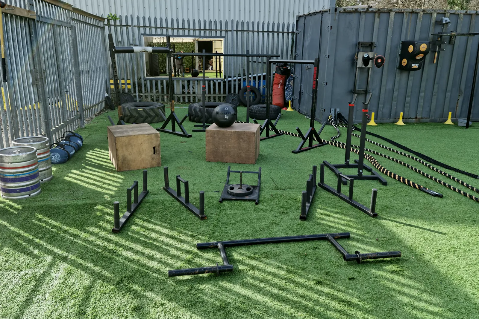 The outdoor gym at POWS: plyo boxes, a sled, battle ropes and racks on artificial turf in the sun.
